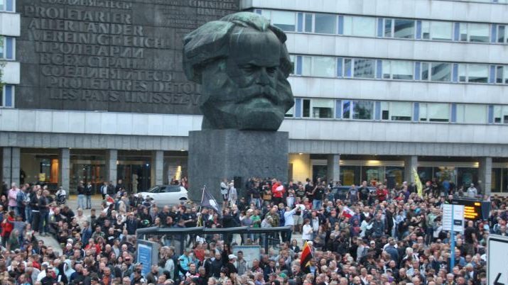 Vor dem Kar Marx Monument in Chemnitz stehen und sitzen Menschen