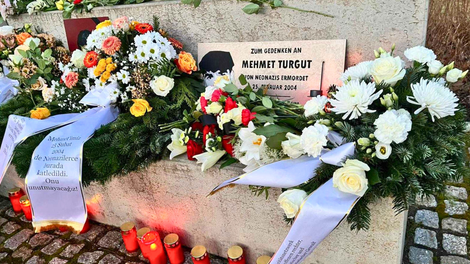 Blumen, Kränze und rote Grablichter liegen an einer Gedenktafel für Mehmet Turgut. Die Tafel erinnert daran, dass er am 25. Februar 2004 von Neonazis ermordet wurde.